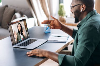 Beyaz kadın meslektaşı ya da kız arkadaşıyla görüntülü konuşma yapan Afrikalı Amerikalı bir adam. İnternette iletişim uygulaması ve dizüstü bilgisayar kullanıyor. Evde oturuyor. Çevrimiçi video toplantısı