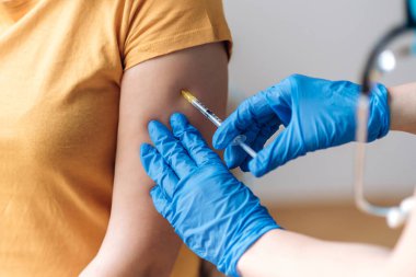 Doktorun koruyucu eldiven giyip laboratuvardaki bir hastaya bir doz aşı verirken yakın plan çekimleri. Koronavirüs aşısı enfeksiyonu. Kovid 19, bir hemşire koluna aşı enjekte ediyor.