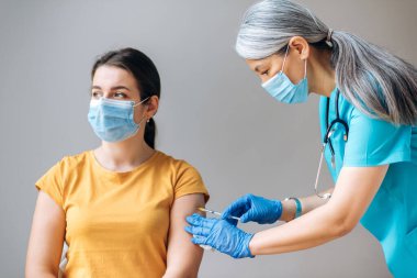 Coronavirus önleme konsepti. Tıbbi maske takan kadın hastanede Coronavirus Covid19 aşısı yaptırıyor. Hasta için aşı yapan orta yaşlı kadın hemşire ya da doktor