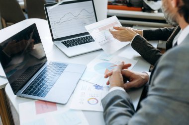 Alet ve belgelerle dolu bir ofis masası. Belgeleri sıralayan, finansal grafikleri öğrenen başarılı iş arkadaşları. İş ortakları ciddi projeler geliştiriyor.