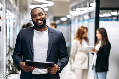 Yaratıcı modern ofis. Kendinden emin Afrikalı Amerikalı bir adam, CEO, programcı ya da tasarımcı, ofiste durup kameraya dostça bakıyor ve gülümsüyor.