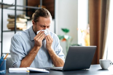 Erkek müdür ya da serbest çalışan ofis masasına oturur, uzaktan çalışır, kağıt mendil kullanır, hapşırır. Kafkasyalı sağlıksız bir adam kendini iyi hissetmiyor, burnu akıyor, dinlenmeye ihtiyacı var.