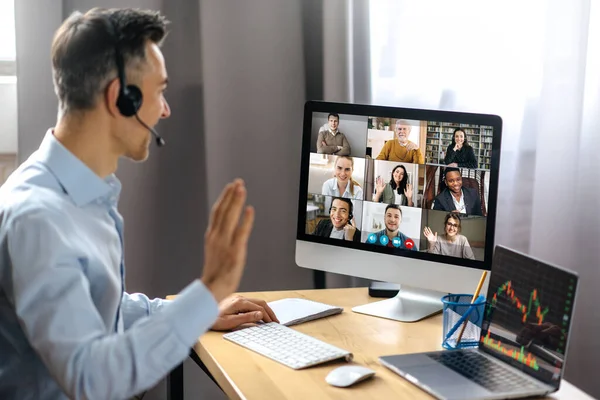 Online conference, video call. Successful adult businessman have conversation with multiracial business colleagues by video call using a computer while sitting at his workplace