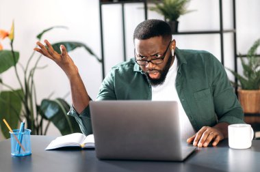 Tatminsiz, çok ırklı siyah adam, erkek serbest çalışan ya da yönetici, dizüstü bilgisayara cesaretini yitirmiş, beklenmedik bir mesaj ya da haber almış, iş yerinde oturuyor.