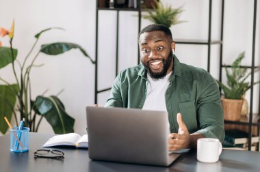 Aşırı mutlu arkadaş canlısı Afrikalı Amerikalı başarılı erkek serbest çalışan ya da iş adamı laptopa mutlu bir şekilde bakıyor, iyi bir mesaj aldı ya da iyi bir anlaşma yaptı.