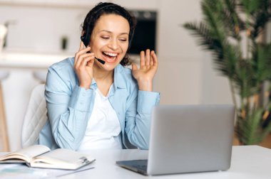 Kendine güvenen, kulaklık takan, serbest çalışan, menajer ya da emlakçı, iş arkadaşı ya da müşterisiyle konferans görüşmesiyle konuşan, el kol hareketi yapan, gülen arkadaş canlısı bir kadın.