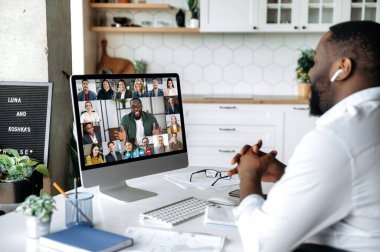Video konferansı. Online toplantı. Zeki Afrikalı Amerikalı iş adamı evdeki çalışma masasına oturur, bilgisayar ekranına bakar, ortaklarıyla video görüşmeleri yapar, bir strateji tartışır.