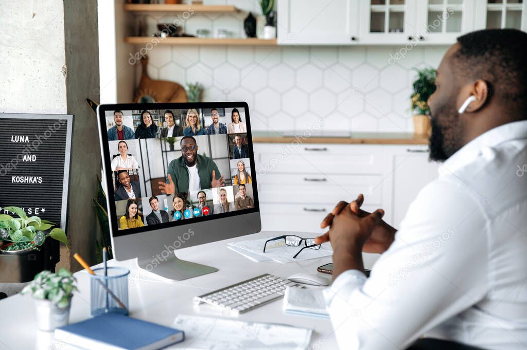 Video conference. online meeting. Intelligent African American business man sits at work desk at home, looks at the computer screen, communicates by video call with his partners, discuss a strategy