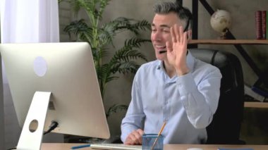 Akıllı başarılı beyaz erkek çalışan, yönetici ya da CEO, resmi gömlek ve kulaklıkla ofiste oturuyor, online iş brifingi veya danışmanlık yapıyor, iş arkadaşlarıyla iletişim kuruyor, gülümsüyor.