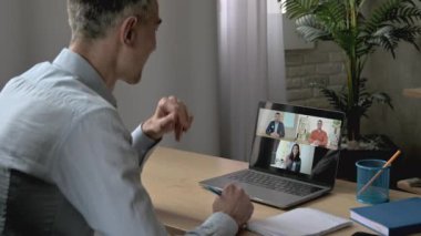 İş konferansı. Beyaz saçlı başarılı iş adamı çalışma masasında otururken dizüstü bilgisayar kullanıyor, iş arkadaşlarıyla video konferansında iletişim kuruyor, finansal konuları tartışıyor.