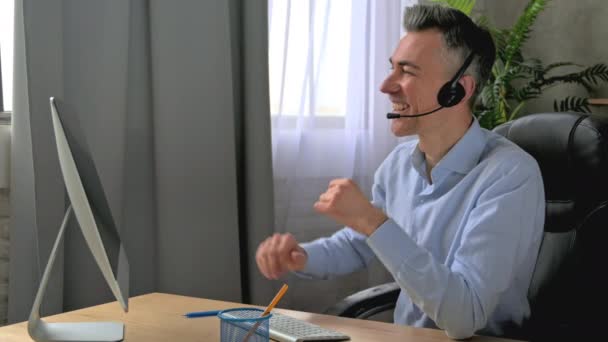 Přátelský kavkazský dospělý muž manažer právník nebo podnikatel, ve sluchátkách, sedí na pracovišti, provádí on-line obchodní jednání nebo konzultace, komunikovat s kolegy nebo zákazníkem, úsměv. Video hovor — Stock video