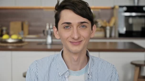 Close-up video portrait of a handsome attractive blue-eyed caucasian guy, student or freelancer. Stylish young man in a shirt looking and smiling friendly at camera, standing indoors. Homosexual guy — 图库视频影像