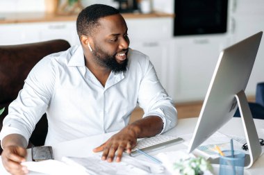 Arkadaş canlısı, kendinden emin, genç, Afrikalı, Amerikalı iş adamı, üst düzey yönetici ya da avukat, çevrimiçi konferans aracılığıyla iş arkadaşlarıyla sohbet ediyor, çevrimiçi konferans izliyor, gülümsüyor.