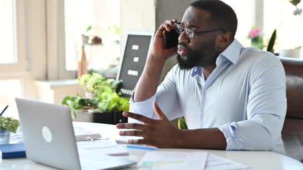 Exitoso ocupado influyente líder empresarial afroamericano, abogado o gerente, en ropa formal, se sienta en el escritorio, utiliza el teléfono celular, habla con el cliente por teléfono inteligente, mientras que el proceso de trabajo — Vídeo de stock