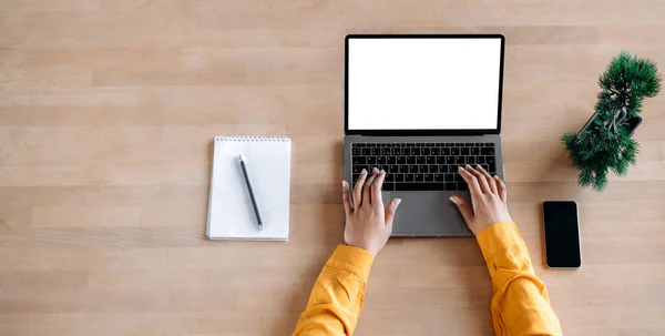 Na stole stojí otevřený notebook s prázdnou bílou obrazovkou, ženské ruce afroameričanky píšou na klávesnici, nedaleko leží notepad, smartphone a květináč. Kopírovat prostor — Stock fotografie