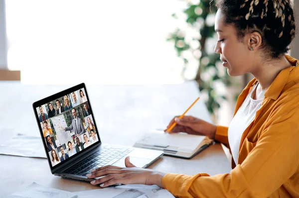 Belső eligazítás, konferencia. Az afro-amerikai női menedzser kommunikál az üzleti csapattal videohívás közben, pénzügyi webináriumot hallgat, jegyzetel a laptop képernyőjén oktató és multiracionális emberek — Stock Fotó