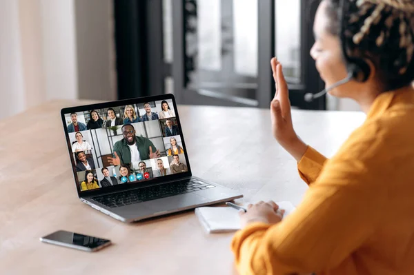 Online business group brainstorm by video conference. Side-view of african american young woman, kommuniserer med forretningspartnere ved hjelp av videosamtaler bruker laptop, multi-rasistiske kolleger på laptop screen stockfoto