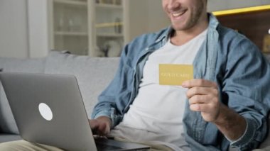 Günlük giysiler içindeki mutlu beyaz adam, dizüstü bilgisayar ve kredi kartını koltukta otururken, online alışverişleri öderken ya da mal teslimatını yaparken kullanıyor, kart detaylarını giriyor