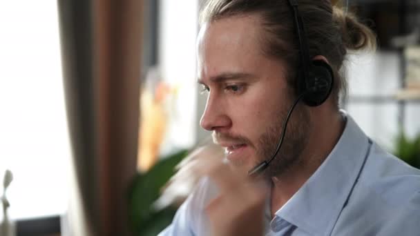 Close-up de bonito barbudo cara caucasiano amigável, operador de call center, serviço de suporte, líder de negócios, realiza consulta distante usa fone de ouvido, conversa com o cliente por chamada on-line — Vídeo de Stock