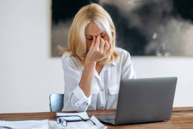 Kafkasyalı, olgun sarışın, CEO, menajer ya da serbest çalışan, beyaz gömlekli, dizüstü bilgisayarla çalışmaktan sıkılmış, stres yaşamaktan sıkılmış, işe ara vermiş, elleriyle gözlerini ovuyor, baş ağrısı var.