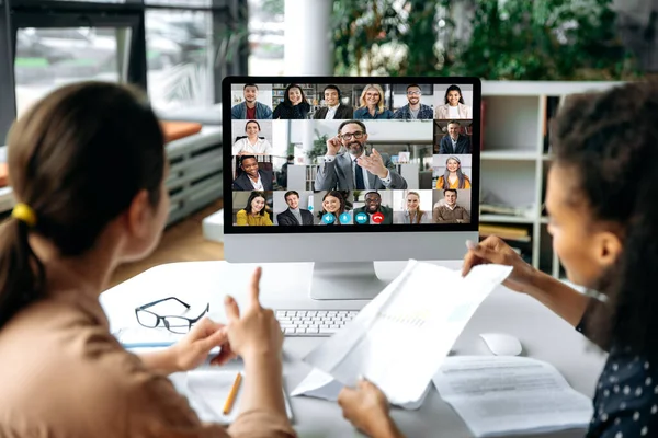 Virtual pertemuan online, panggilan video. Lihat lebih dari bahu dua perempuan ke layar komputer dengan pemimpin bisnis dan tim yang sukses, mengobrol melalui konferensi video, membahas isu-isu kerja, strategi — Stok Foto