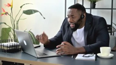 Sinirli Afro-Amerikan iş adamı, yönetici, video konferansı yoluyla tatsız bir konuşma yapıyor. Laptop kullanıyor, iş yerinde oturuyor, çalışanlarla anlaşmazlık yaşıyor, asık surat ifadesi takınıyor.