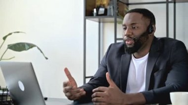 Dost canlısı özgüvenli Afrikalı Amerikalı iş adamı, danışman ya da yönetici, bilgisayar başında çalışan, video konferans yoluyla çalışan veya müşteriyle iletişim kuran, elleriyle hareket eden, gülümseyen