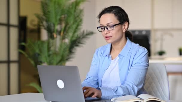 Mujer madura de raza mixta cansada, con exceso de trabajo, usando gafas, independiente, secretaria o gerente, tomó un descanso, se sienta en el escritorio, estresada y cansada de trabajar en la computadora, se quita las gafas, masajea los ojos — Vídeos de Stock