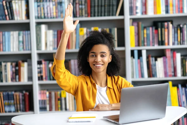 Smart afroamerikansk kvinnlig student på en föreläsning sitter vid ett skrivbord, vet svaret på en fråga, lyfter handen, vill svara, tittar på kameran, ler, kunskap och utbildning koncept — Stockfoto