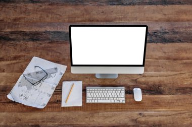 Sunumunuz için boş beyaz ekranlı bir bilgisayar monitörünün üst görüntüsü ahşap bir masanın üzerinde duruyor, tasarım çizimi, not defteri ve gözlük yakınlarda. Model, boşluk konseptini kopyala