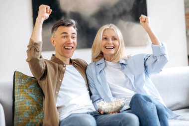 Neşeli orta yaşlı evli bir çift, karı koca, rahat rahat koltuklarda oturuyor, TV şovu, film ya da futbol izliyor, patlamış mısır yiyor, el kol hareketi yapıyor, kazanmanın sevincini yaşıyor.
