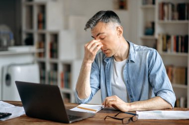 Yorgun, kır saçlı, yaşlı, beyaz, menajer ya da serbest çalışan, şık giyimli, evden çalışıyor, bir çok işten yorulmuş, stresli, işe ara vermiş, tatile ihtiyacı var, elleriyle gözlerini ovuşturuyor.