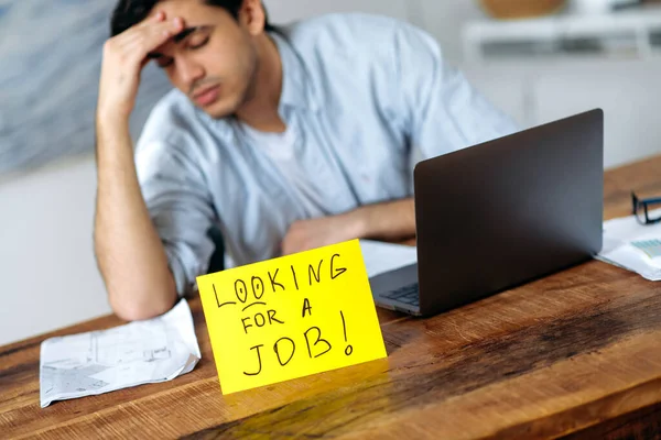 Erschöpfter arbeitsloser hispanischer Typ, sitzt am Tisch, auf dem Tisch steht ein Schild mit der Aufschrift "Suche nach einem Job", in der Hoffnung auf einen Traumjob, Stress, Augen zu, müde vom Suchen — Stockfoto