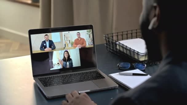 Melihat ke belakang bahu pengusaha Afrika-Amerika yang sukses duduk di meja kerja, menggunakan laptop, berkomunikasi pada konferensi video dengan rekan-rekan, membahas strategi, beragam orang di layar laptop — Stok Video