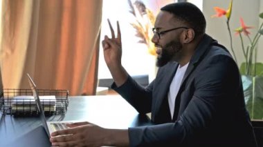 Çevrimiçi video bağlantısı. Mutlu gülümseyen Afrikalı Amerikalı adam, iş adamı ya da menajer, iş arkadaşlarıyla video iletişimi, telekomünikasyon konsepti ve video aracılığıyla sohbet için dizüstü kullanıyor.