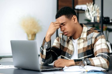 Yorgunluktan bitap düşmüş başarılı Latin erkek serbest çalışan ya da ofis çalışanı, iş yerinde gözleri kapalı oturur, gözlerini ovuşturur, baş ağrısı, stres ve fazla mesai yorgunluğu hisseder, dinlenmeye ihtiyacı vardır.