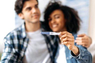 Neşeli, bulanık genç, çok ırklı evli çift iyi haberlerin tadını çıkarıyor, ebeveyn olmaya hazırlanıyor, mutlu Afrikalı Amerikalı kız pozitif bir hamilelik testi yapıyor.