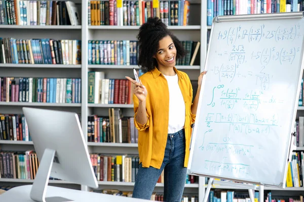 Happy smart selbstbewusst schöne afroamerikanische Lehrerin in stilvoller Kleidung, steht in der Nähe des Whiteboards, leitet eine Online-Lektion, kommuniziert mit den Schülern über eine Videokonferenz, per Computer — Stockfoto