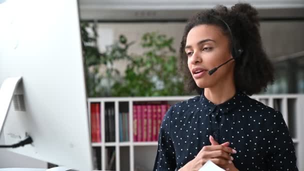 African American friendly νεαρή γυναίκα με ακουστικά, εργαζόμενος τηλεφωνικό κέντρο, σύμβουλος, επιχειρηματικό πρόσωπο, επικοινωνούν με τους συναδέλφους ή τους πελάτες μέσω τηλεδιάσκεψης, διεξάγει διαβουλεύσεις, online ενημέρωση — Αρχείο Βίντεο