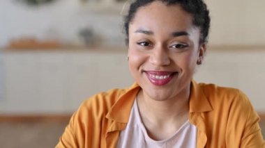 Güzelim Afro-Amerikan mutlu genç bir kadının video portresi. Rastgele giyinmiş, serbest çalışan ya da bayan öğrenci. Dostane bir gülümsemeyle doğrudan kameraya bakıyor.