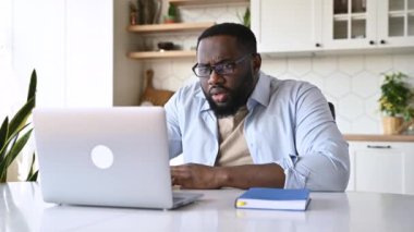Şaşırmış afro-amerikan sakallı adam, işletme yöneticisi, serbest çalışan, masasında oturuyor, gözlüğünü çıkarırken bilgisayarına bakıyor, beklenmedik haberler okuyor veya kötü mesajlar okuyor.