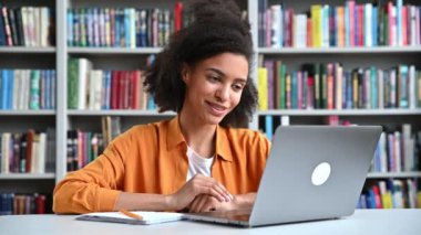 Çevrimiçi iletişim. Kendine güvenen zeki Afro-Amerikan stil kızı, üniversite kütüphanesindeki bayan öğrenci dizüstü bilgisayar kullanıyor, video konferansı arkadaşı ya da sınıf arkadaşı ile konuşuyor, el kol hareketi yapıyor.