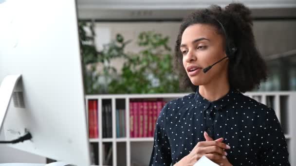 Mujer joven afroamericana amigable con auriculares, trabajador del centro de llamadas, consultor, persona de negocios, comunicarse con colegas o clientes a través de videoconferencia, lleva a cabo consultas, información en línea — Vídeos de Stock