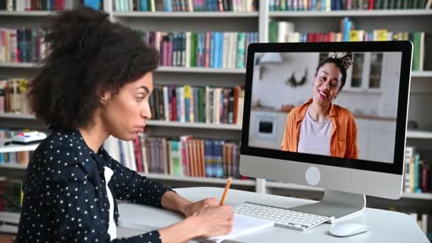 มุมมองด้านข้างของนักเรียนหญิงชาวแอฟริกันอเมริกันที่ฉลาดในระหว่างการบรรยายออนไลน์ ครูสอนภาษาแอฟริกันอเมริกันหญิงทําบทเรียนออนไลน์ นักเรียนหญิงจดบันทึก การฝึกอบรมออนไลน์, โทรวิดีโอ — วีดีโอสต็อก