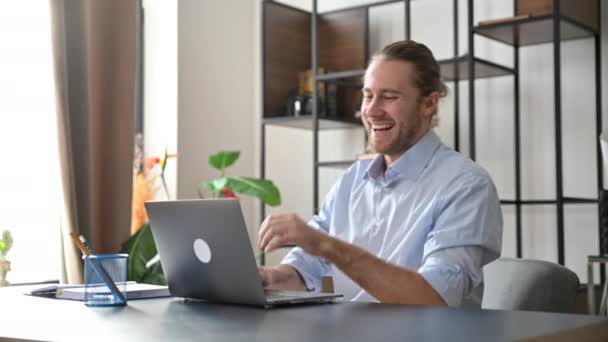 Lachen aantrekkelijke jonge man, freelancer of manager, is ontspannen op het werk met benen gegooid op tafel. Moderne man maakt gebruik van laptop, surfen op het internet, zoekt naar ideeën, ontspant tijdens het werk — Stockvideo