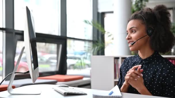 Přátelská africká americká mladá žena se sluchátky, pracovnice call centra, konzultantka, podnikatelka, mluví s kolegy nebo klienty pomocí videohovoru, provádí online konzultace — Stock video