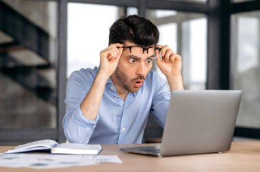 Şaşırmış Kafkasyalı ofis çalışanı ya da girişimci iş yerinde oturur, dizüstü bilgisayara bakar, bardaklarını kaldırır, beklenmedik haberler alır, zafer kazanır, büyük bir kar elde eder.