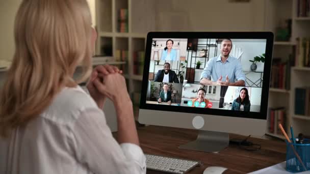 Διαδικτυακή επικοινωνία. View over a womans shoulder at a computer screen with various business people συγκεντρώθηκαν σε ένα ομαδικό online συνέδριο από διάφορα μέρη του κόσμου για να συζητήσουν θέματα εργασίας — Αρχείο Βίντεο