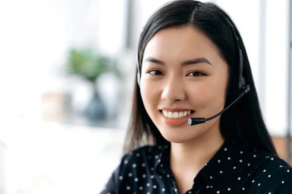 Close-up portrait of beautiful confident long haired young asian woman in headset, freelancer, call center worker or consultant, wearing black stylish shirt, looks directly at camera, smiling friendly — Stock Photo, Image