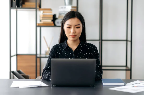 Güzel başarılı Asyalı genç iş kadını, menajer, CEO, şık kıyafetler içinde, ofiste oturuyor, dizüstü bilgisayar kullanıyor, eğitim videoları izliyor, müşteri ya da çalışanla mesajlaşıyor, ekrana bakıyor. — Stok fotoğraf